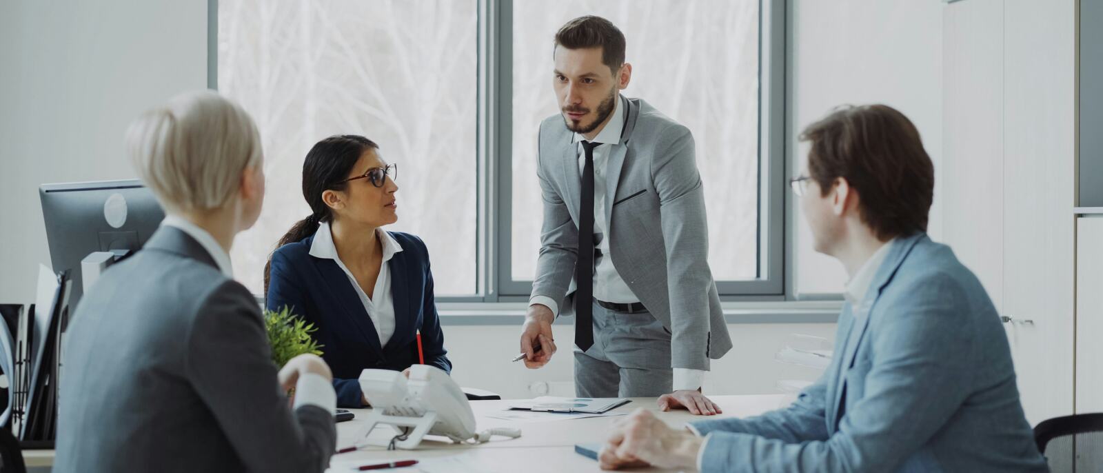 A colleague standing to address others around a meeting table