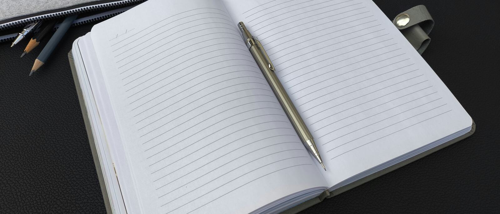An open notebook and pen beside a pencil case