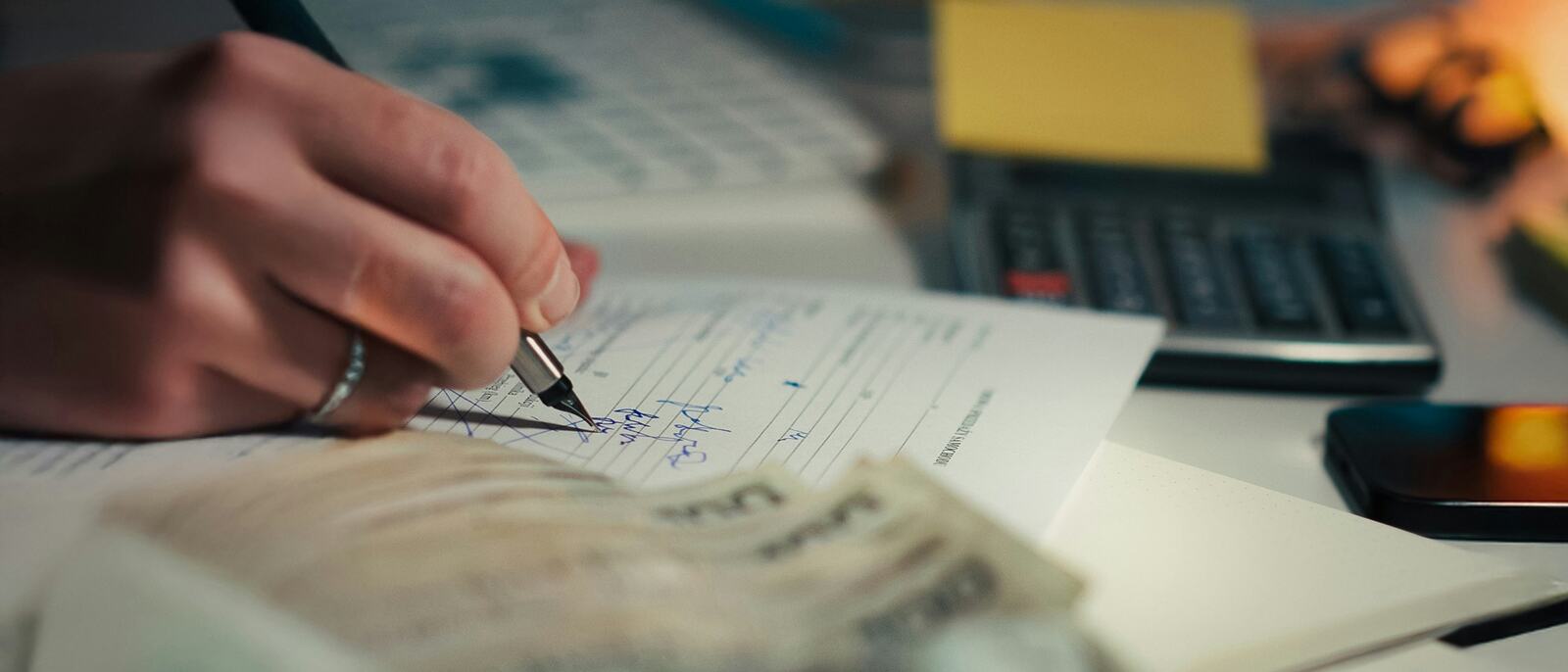 Hand writing in a notebook beside cash and a calculator